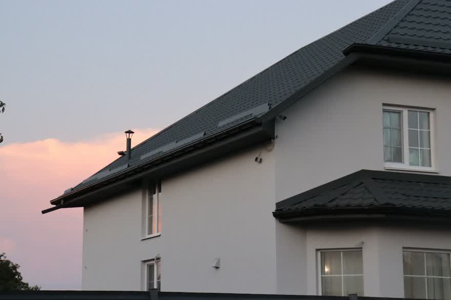 Wohnhaus mit dunklem Dach, Solarkollektoren und Dachrinne